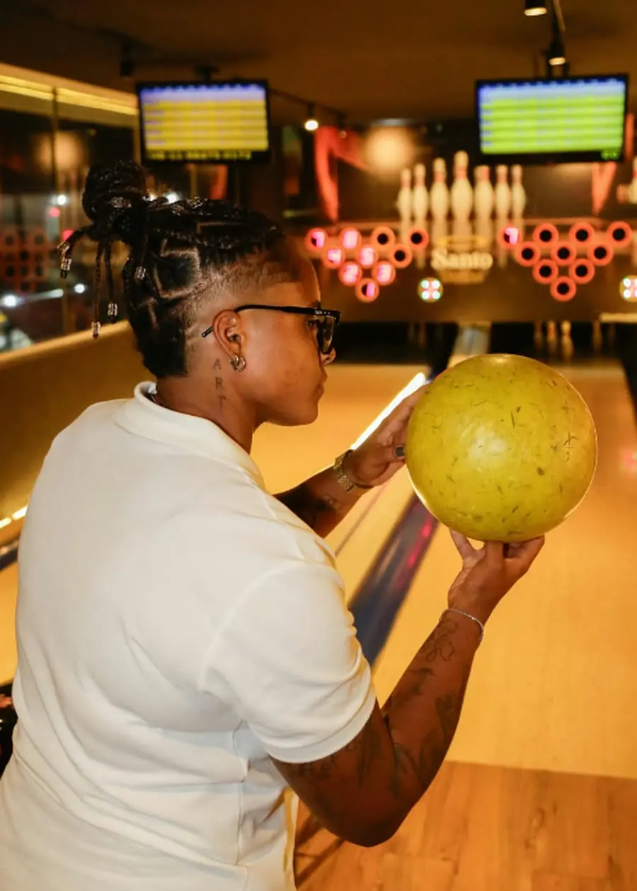 Cliente jogando boliche na pista do Santo Strike, com os pinos e o letreiro em neon ao fundo